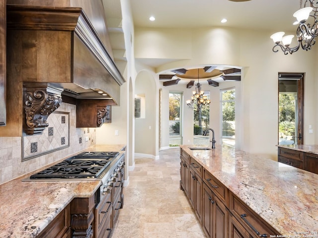 kitchen with pendant lighting, sink, backsplash, a chandelier, and light stone countertops