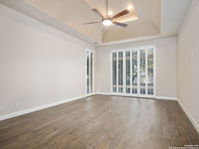 empty room with dark hardwood / wood-style flooring, a raised ceiling, and ceiling fan