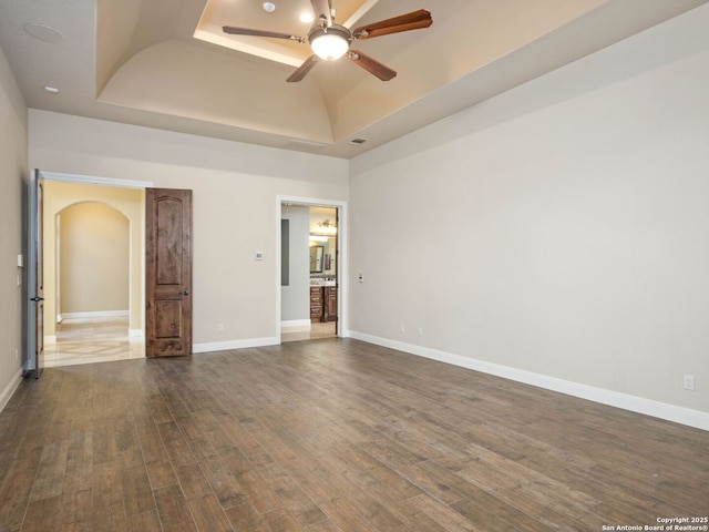 empty room with a raised ceiling, a towering ceiling, ceiling fan, and dark hardwood / wood-style floors