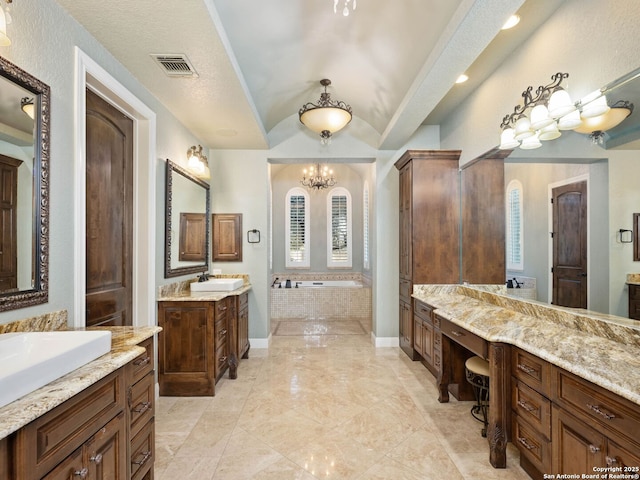 bathroom featuring an inviting chandelier, vaulted ceiling, a textured ceiling, vanity, and tiled tub