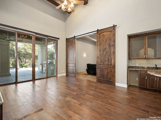 unfurnished living room featuring a towering ceiling, sink, ceiling fan, a barn door, and beam ceiling