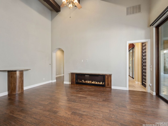 unfurnished living room featuring beamed ceiling, a high ceiling, and dark wood-type flooring