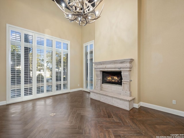 unfurnished living room with a notable chandelier, a high end fireplace, dark parquet floors, and a high ceiling