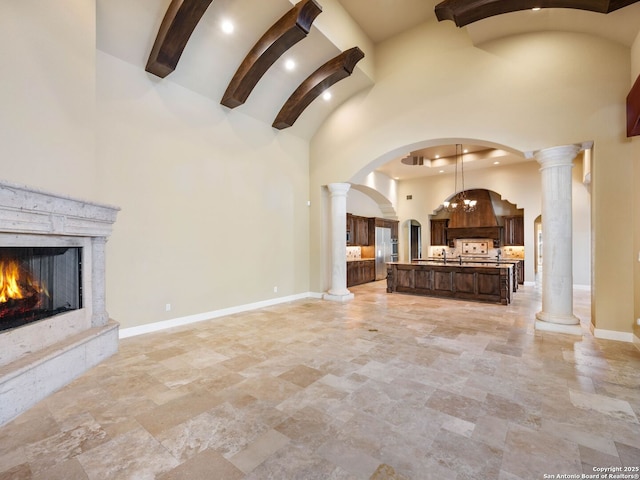 unfurnished living room with a high end fireplace, decorative columns, and a high ceiling