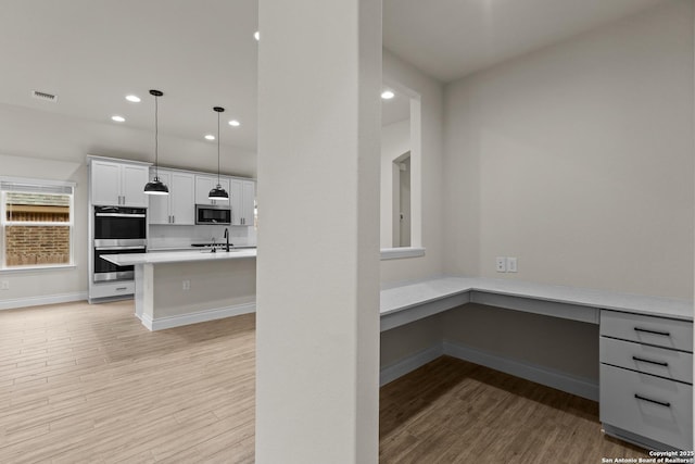 kitchen featuring decorative light fixtures, built in desk, light hardwood / wood-style flooring, stainless steel appliances, and white cabinets