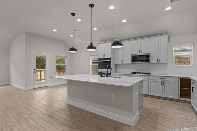 kitchen featuring pendant lighting, sink, vaulted ceiling, and an island with sink