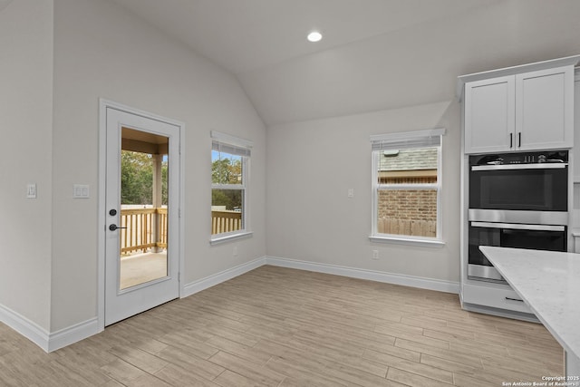 kitchen featuring vaulted ceiling, double oven, a healthy amount of sunlight, light stone countertops, and white cabinets