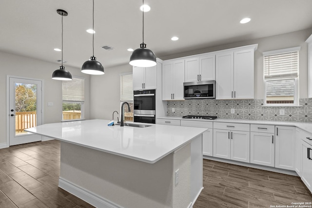 kitchen with stainless steel appliances, white cabinetry, a kitchen island with sink, and pendant lighting