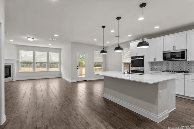 kitchen with sink, decorative light fixtures, stainless steel appliances, a kitchen island with sink, and white cabinets