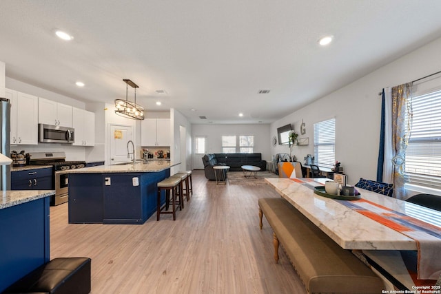 kitchen with a kitchen bar, a center island with sink, pendant lighting, stainless steel appliances, and white cabinets