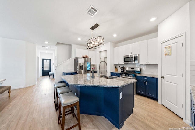 kitchen featuring appliances with stainless steel finishes, an island with sink, sink, white cabinets, and blue cabinetry