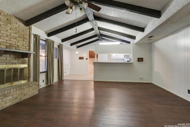 unfurnished living room with a fireplace, lofted ceiling with beams, dark hardwood / wood-style flooring, ceiling fan, and a textured ceiling