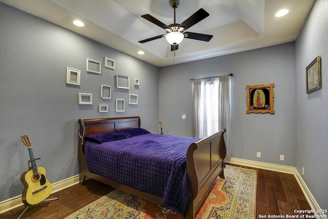 bedroom with dark wood-type flooring, ceiling fan, and a raised ceiling