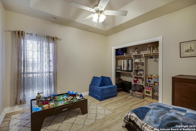 bedroom with a tray ceiling, a closet, ceiling fan, and light wood-type flooring