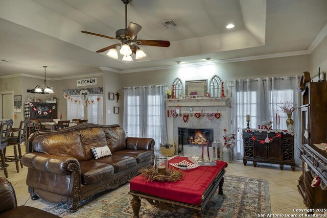 living room with light tile patterned floors, ceiling fan, a tray ceiling, a fireplace, and ornamental molding