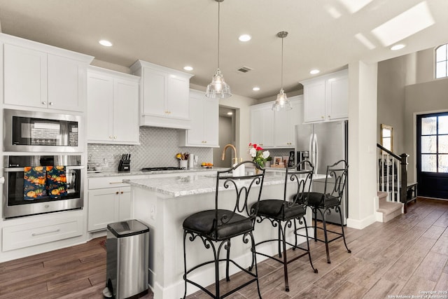 kitchen featuring a kitchen island with sink, white cabinets, and decorative light fixtures