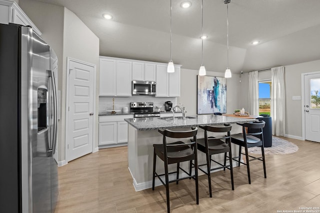 kitchen featuring lofted ceiling, appliances with stainless steel finishes, hanging light fixtures, white cabinets, and a center island with sink