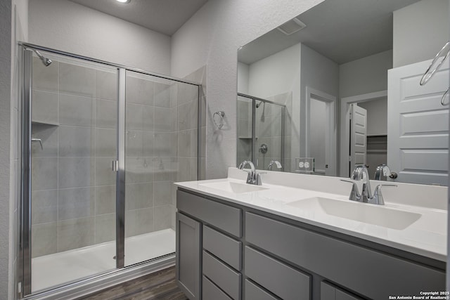 full bathroom with double vanity, a stall shower, a sink, and wood finished floors