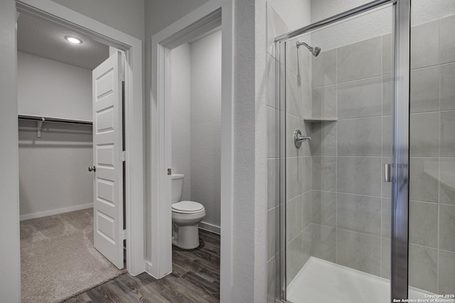 full bath with toilet, a shower stall, a spacious closet, and wood finished floors