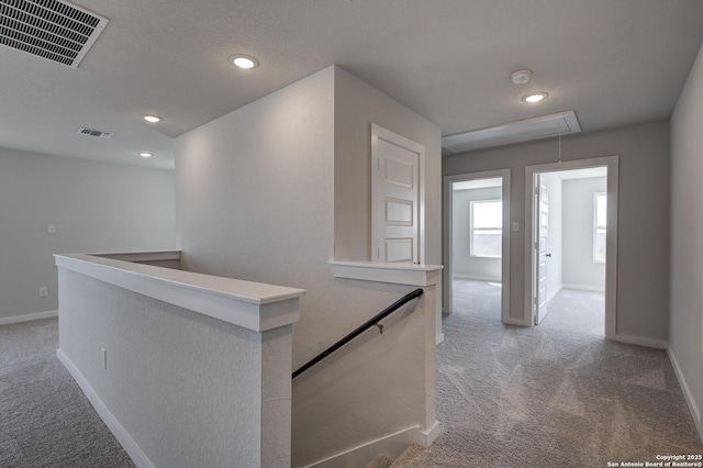 hallway featuring light carpet, an upstairs landing, baseboards, visible vents, and attic access