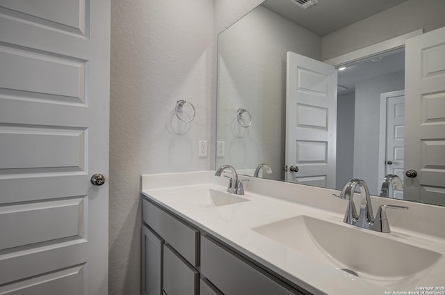 bathroom with a textured wall, double vanity, a sink, and visible vents