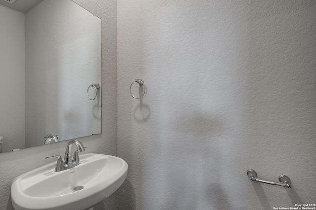 half bath featuring a textured wall and a sink