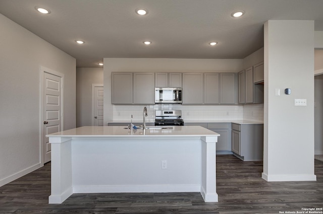 kitchen featuring decorative backsplash, an island with sink, stainless steel appliances, gray cabinetry, and a sink