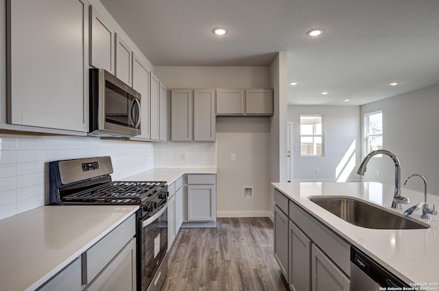 kitchen featuring appliances with stainless steel finishes, a sink, gray cabinetry, and wood finished floors