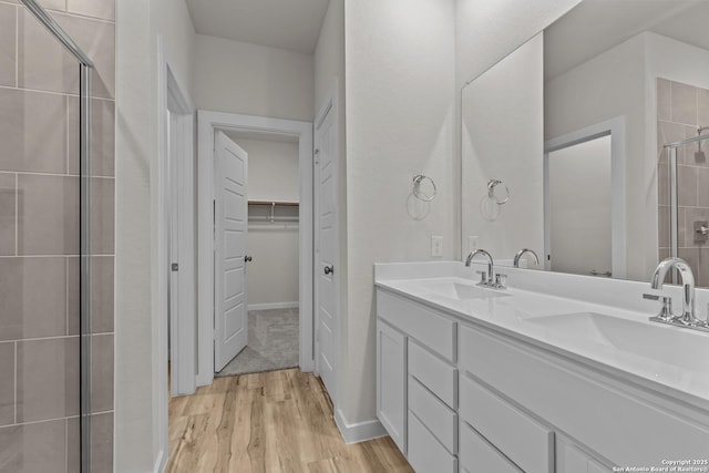 full bathroom with a stall shower, a walk in closet, a sink, and wood finished floors