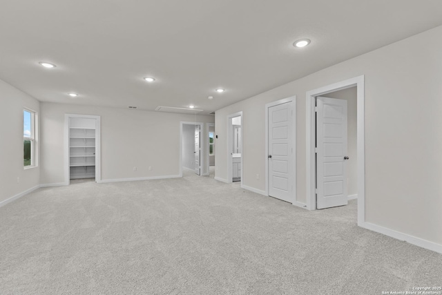 spare room with attic access, light colored carpet, and baseboards