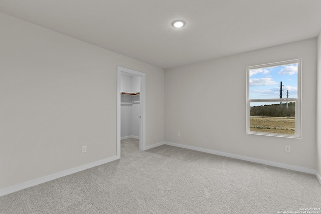 unfurnished bedroom with a closet, light carpet, a spacious closet, and baseboards