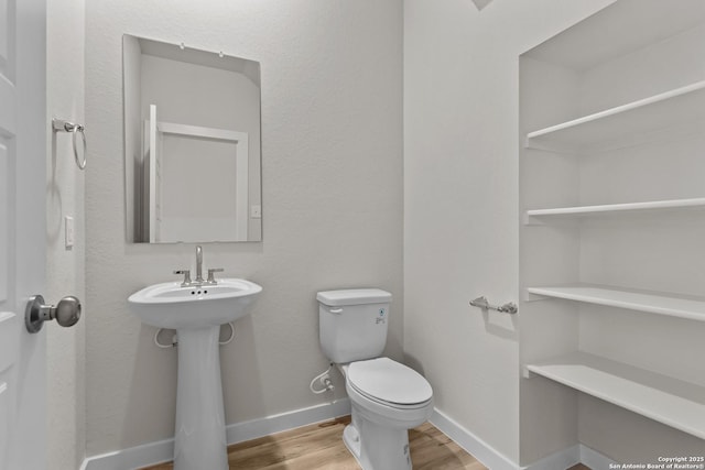 half bath featuring a sink, wood finished floors, toilet, and baseboards