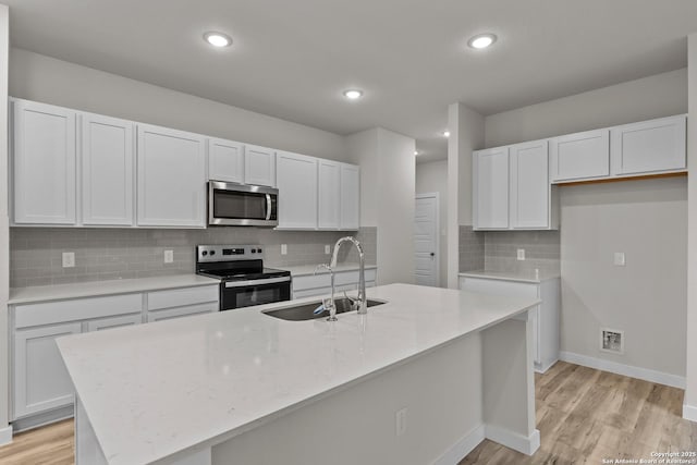 kitchen with stainless steel appliances, white cabinets, a sink, and a center island with sink