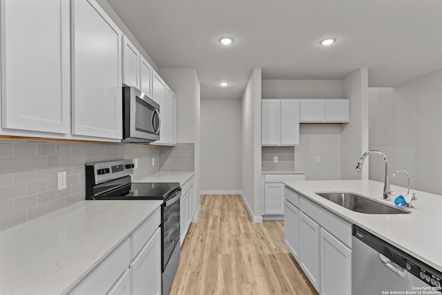 kitchen featuring light stone counters, stainless steel appliances, light wood-style floors, white cabinets, and a sink