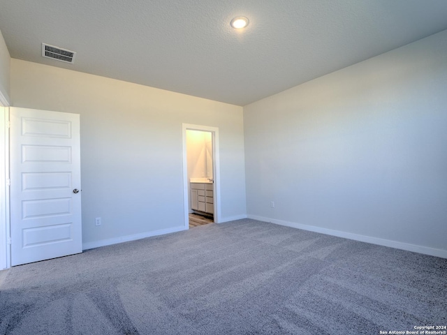 unfurnished bedroom with ensuite bathroom, carpet floors, and a textured ceiling