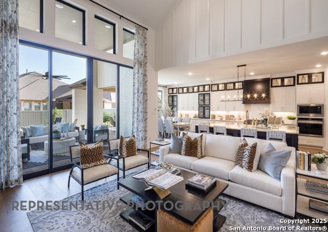 living room featuring a high ceiling, plenty of natural light, ceiling fan with notable chandelier, and light hardwood / wood-style floors