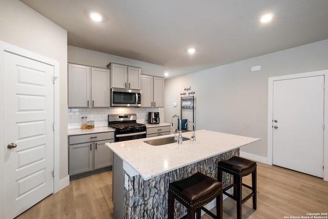 kitchen featuring stainless steel appliances, sink, gray cabinetry, and a kitchen island with sink