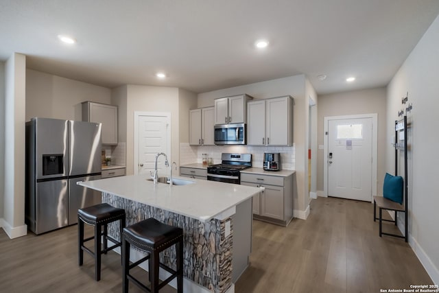 kitchen with sink, gray cabinetry, stainless steel appliances, an island with sink, and light wood-type flooring