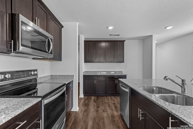 kitchen with stainless steel appliances, sink, light stone counters, and dark hardwood / wood-style floors