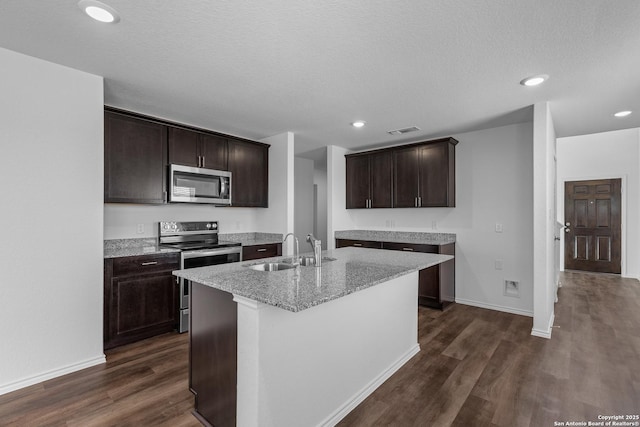 kitchen with dark brown cabinetry, sink, an island with sink, stainless steel appliances, and light stone countertops