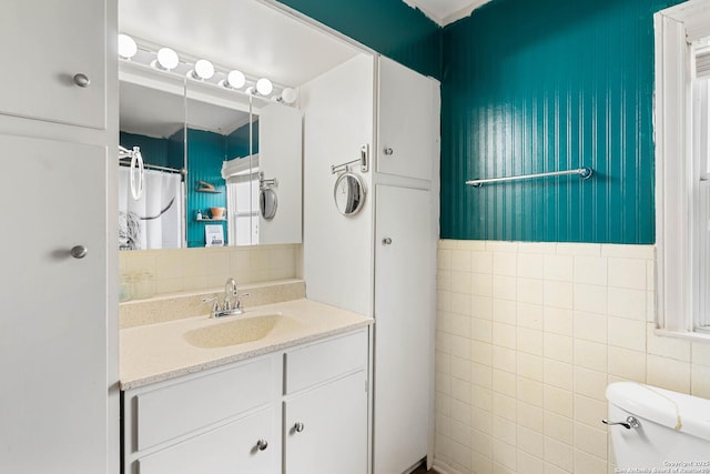 bathroom with vanity, toilet, a shower with shower curtain, and tile walls