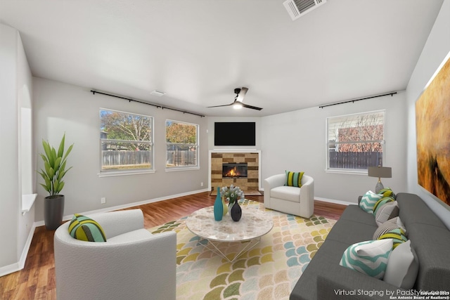 living room with a tile fireplace, wood-type flooring, and ceiling fan