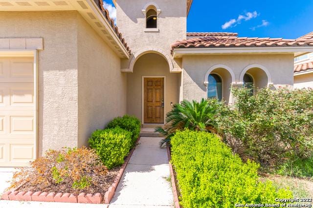 doorway to property with an attached garage, a tile roof, and stucco siding