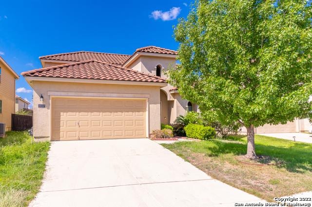 mediterranean / spanish house with a garage, central AC, a tile roof, driveway, and stucco siding