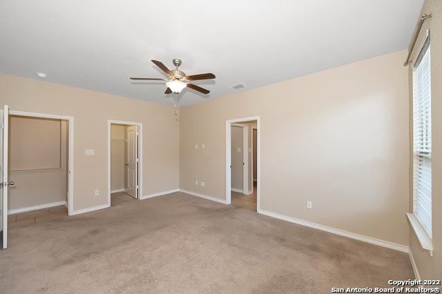 unfurnished bedroom with light carpet, a spacious closet, a closet, and ceiling fan