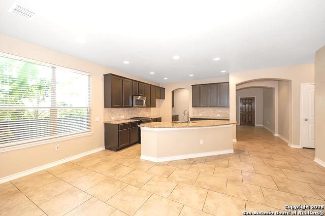 kitchen with light tile patterned flooring, sink, tasteful backsplash, dark brown cabinets, and a kitchen island with sink