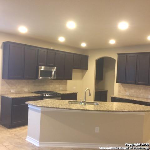 kitchen with an island with sink, light stone countertops, sink, and light tile patterned floors