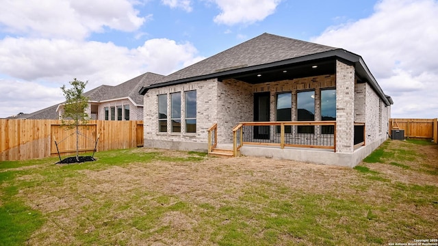 rear view of property featuring a fenced backyard, roof with shingles, brick siding, central air condition unit, and a yard