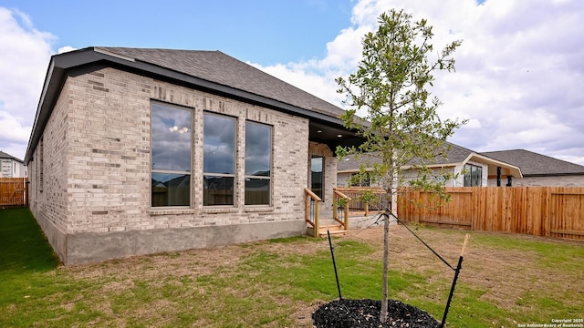 rear view of house featuring brick siding, a fenced backyard, roof with shingles, and a yard