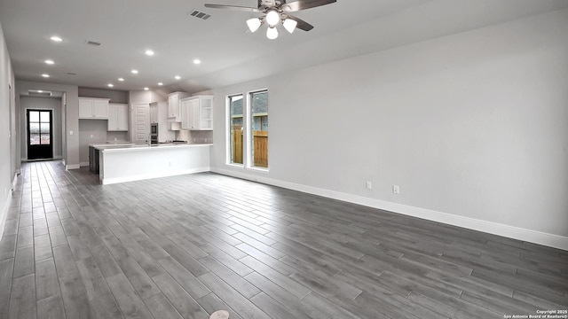 unfurnished living room with a ceiling fan, baseboards, visible vents, and dark wood-type flooring